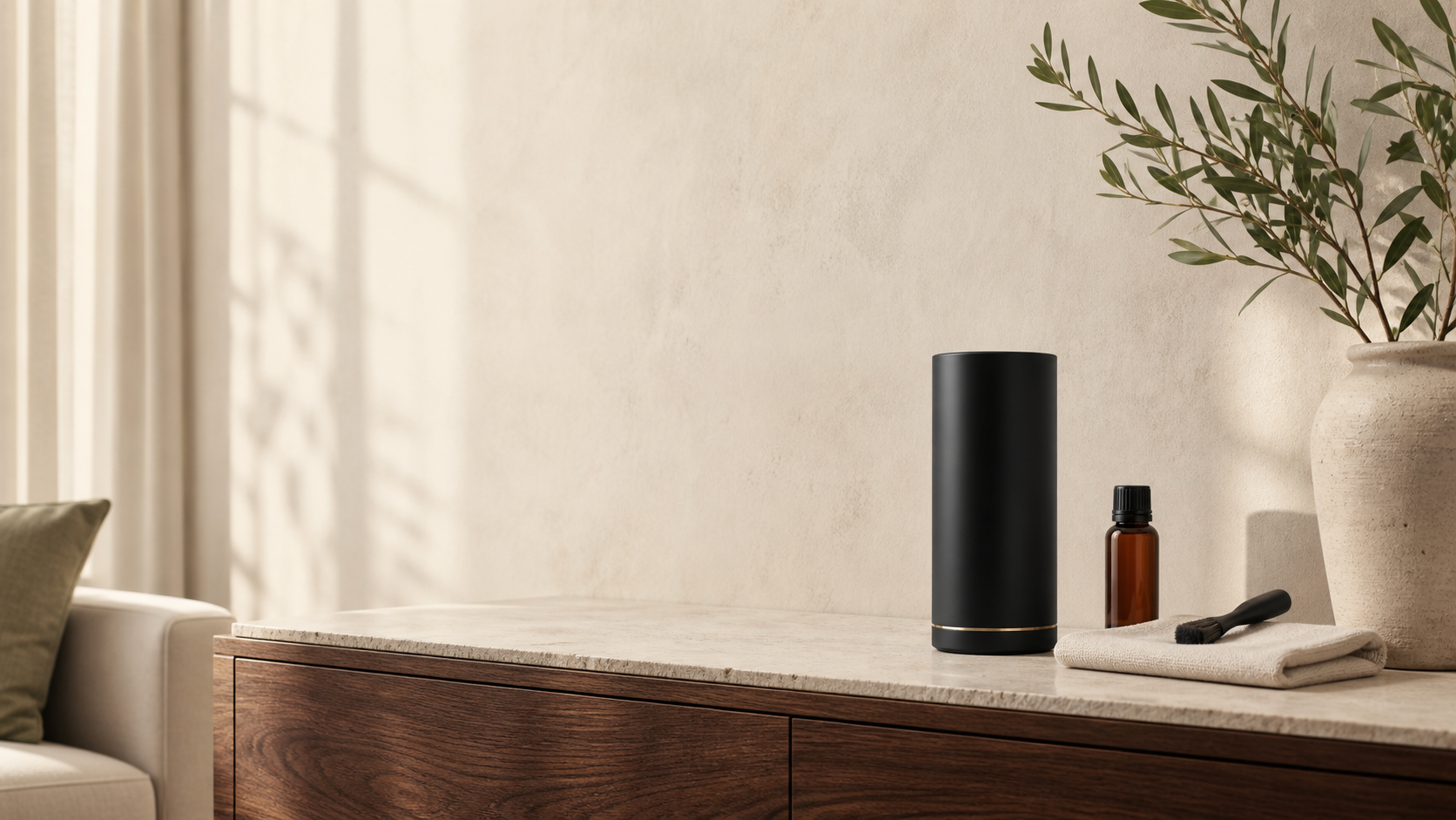 A matte black scent diffuser with an amber bottle and simple care tools on a warm interior console