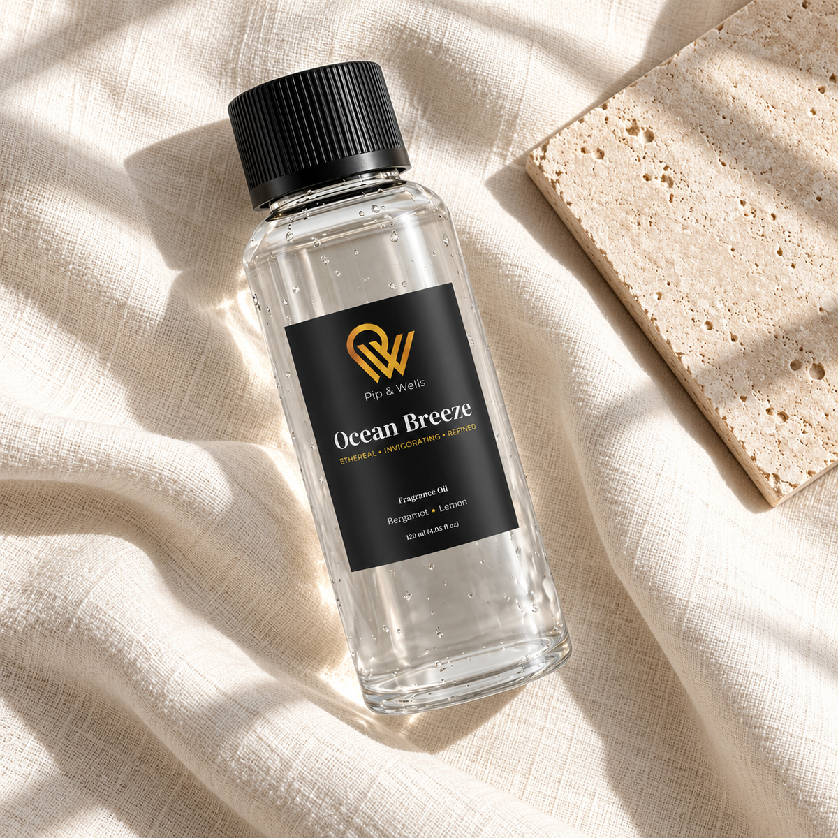 Flacon d’huile parfumée Pip & Wells Ocean Breeze de 120 ml sur du lin clair, à côté d’un carreau de pierre texturé